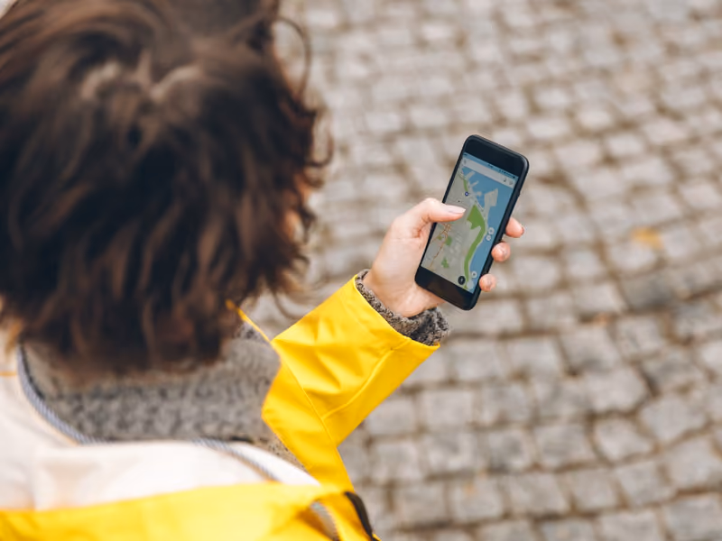 View from above of brunette female being lost in unknown place trying to find route using online map in her phone