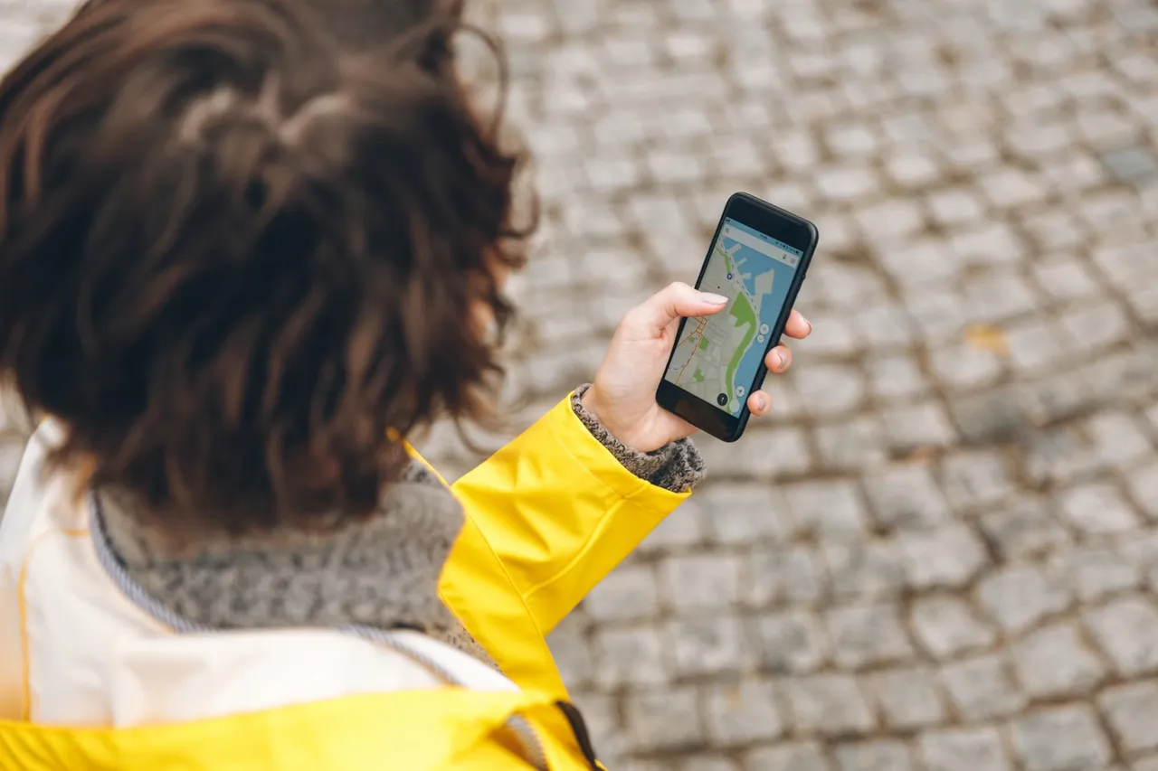 View from above of brunette female being lost in unknown place trying to find route using online map in her phone