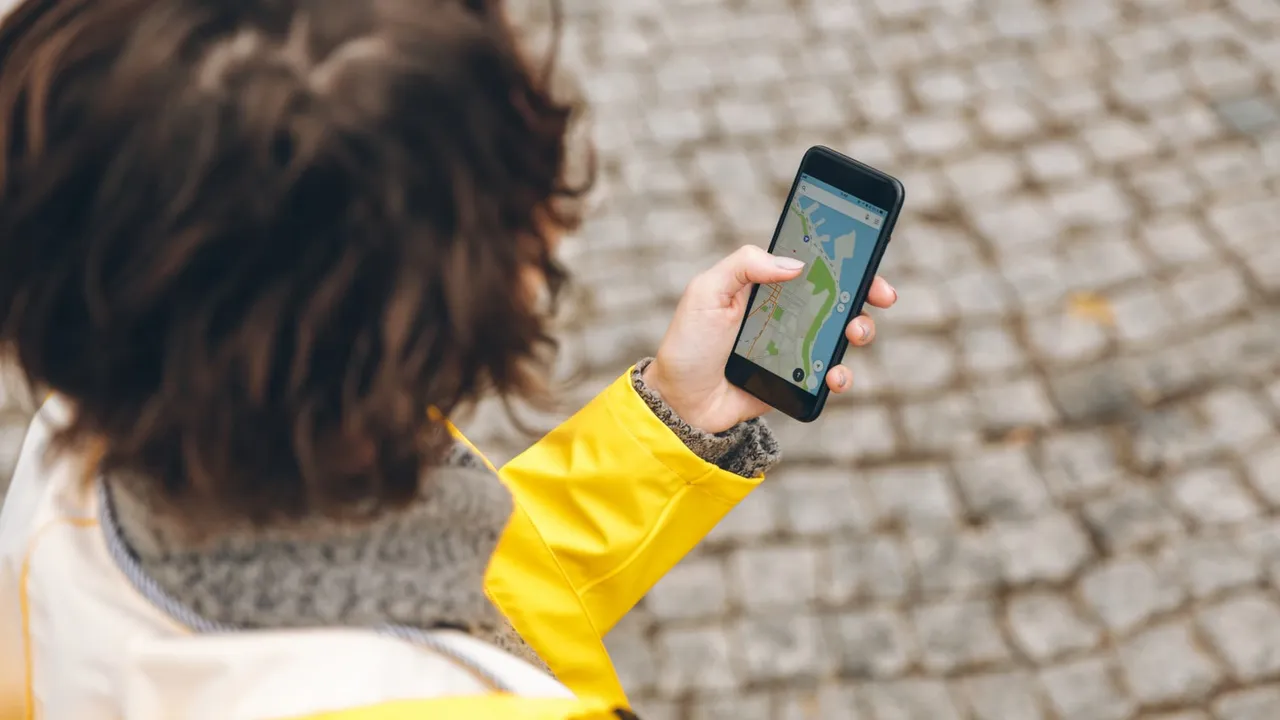 View from above of brunette female being lost in unknown place trying to find route using online map in her phone